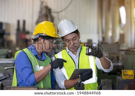 Two workers in production plant as team discussing, industrial scene in background, working together manufacturing activities