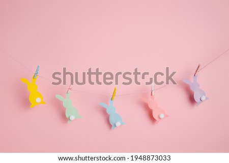 Cute colorful bunnies fastened by a clothespin and hanging on the clothes rope line against pastel pink background. Creative Easter concept.