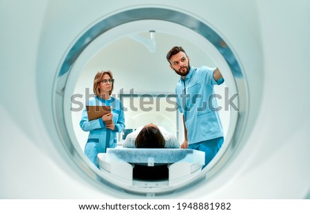 The patient lies on CT or MRI, the bed is moved inside the machine, scanning her body and brain under the supervision of a doctor and a radiologist. In a medical laboratory with high-tech equipment. Royalty-Free Stock Photo #1948881982