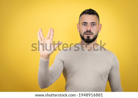 Handsome man with beard wearing sweater over yellow background doing hand symbol
