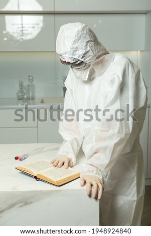physician wearing covid PPE suit uniform, inhaler, gloves and protective glass reads a book