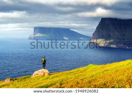 Lonely tourist looks at foggy islands in Atlantic ocean from Kalsoy island, Faroe Islands, Denmark. Landscape photography
