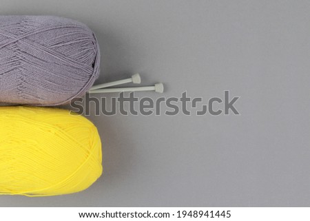 Showing off the colors of 2021-gray and yellow. Yellow and gray yarn and knitting needles on a gray background.The concept of manual labor and a favorite hobby.Top view. Flatlay.Copyspace