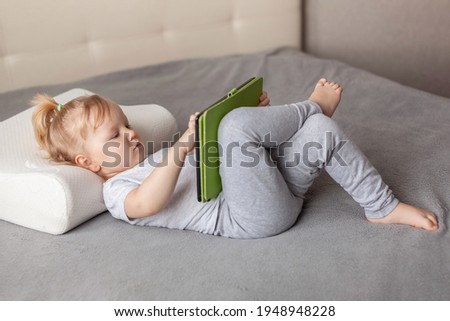 Little cute girl lying on the bed and using a digital tablet laptop notebook