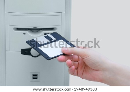 A hand inserts a floppy disk into a personal computer. Retro technology.