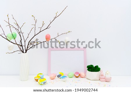 Front view of Easter holiday composition. Hand painted colorful eggs in trendy colors, geometric vase with moss, confetti in eggshell, twigs, pink Easter bunny. Photo frame mockup for Easter design