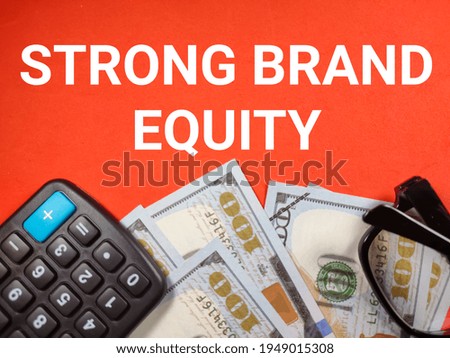 Business concept.Text STRONG BRAND EQUITY with glasses,banknote and calculator on red background.
