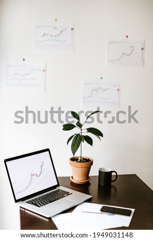 study desk of investment manager with with green plant and cup of coffee. stocks price graph data trend background. 
