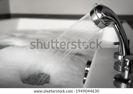 Filling water into bathtub with soap foam on surface, preparation for spa massage - relaxation concept. Close-up and selective focus at the shower head's part, object photo.