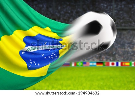 Soccer ball in fast motion in front of the Brazilian flag waving in a spiffy way in a football arena