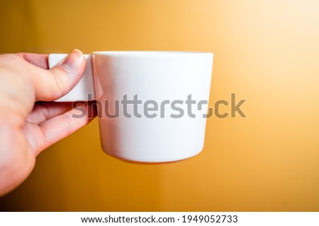 A woman's hand holds a white coffee cup on an orange background.