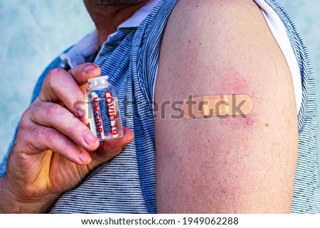 a man with an injection patch on his arm holds an ampoule with the inscription david 19 vaccine concept vaccination medicine pharmacy. High quality photo