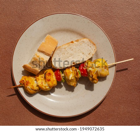 White plate with a chicken skewer and a couple of bread slices on a red background.