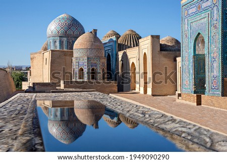 Mausoleums and domes of the historical cemetery of Shahi Zinda and their reflections in puddle, Samarkand, Uzbekistan. Royalty-Free Stock Photo #1949090290