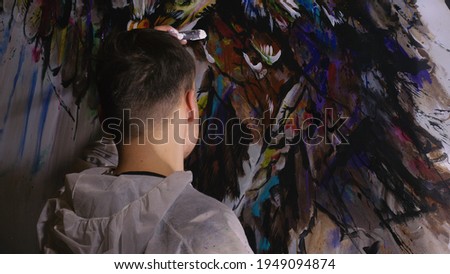 Artist designer draws an eagle on the wall. Craftsman decorator paints picture with acrylic oil color. Painter painter dressed in paint coat. Indoor.