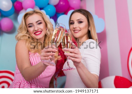 Two young women in pink dresses hold glasses of champagne.
