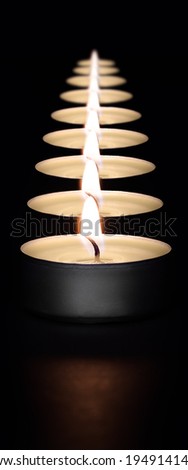 A row of burning candles on a dark background with a flare in the foreground.