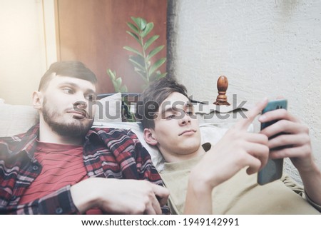 two friends are looking at phone screen while relaxing at home