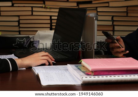 Notebooks are lying on a desk, there are edicational supplies and laptops that are being used by students