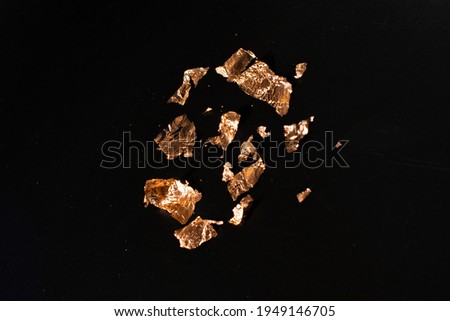 Shiny pieces of gold leaf on a black background. Gold sweat lies on a black table.