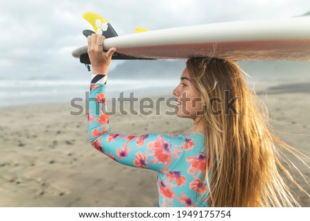 Blonde surfer girl on the beach with surfboard smiling