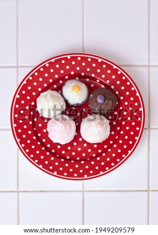 Five cute cupcakes are placed on a red plate with a white dotted pattern.