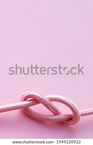 Vertical pastel pink background picture with a rope. A concept for tying the knot, marriage and wedding