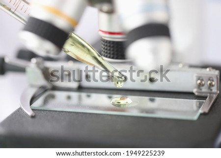 Golden liquid is dripped from pipette onto microscope slide