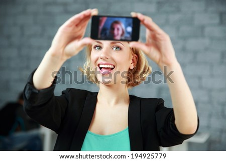 Young laughing woman making a self photo by her smartphone in office