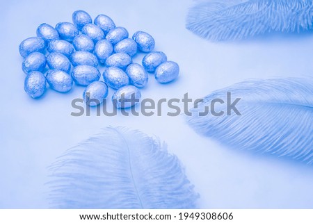 Easter blue light background with chocolate easter eggs wrapped in foil with blue feathers on a light blue background. Easter concept. Aesthetic creative still life composition. Selective focus