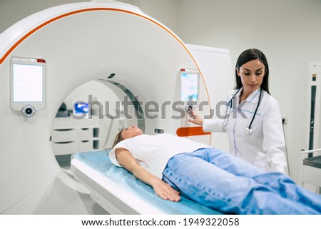 Professional Doctor Radiologist In Medical Laboratory Controls magnetic resonance imaging or computed tomography or PET Scan with Female Patient Undergoing Procedure. Royalty-Free Stock Photo #1949322058