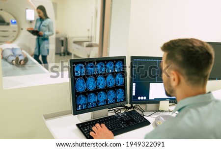 Back view photo of a male doctor sitting near the computer and looking on patient in magnetic resonance imaging machine