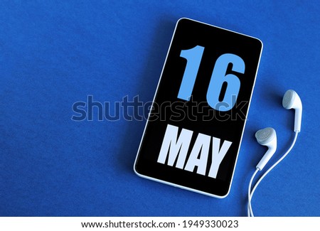 May 16. 16 st day of the  month, calendar date. Smartphone and white headphones on a blue background. Place for your text. Springtime month, day of the year concept.