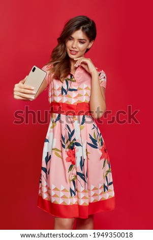 Cheerful young woman doing selfie shot on mobile phone, isolated on a red background.