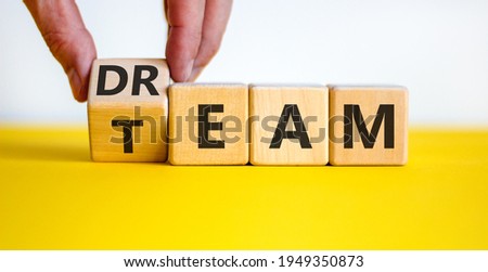 Dream team symbol. Businessman turns the cube and changes the word 'dream' to 'team'. Beautiful yellow table, white background. Business and dream team concept, copy space. Royalty-Free Stock Photo #1949350873