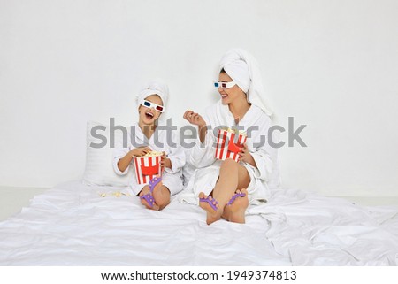 woman with daughter in white bathrobes watching movie