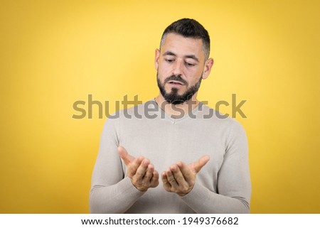 Handsome man with beard wearing sweater over yellow background Smiling with hands palms together receiving or giving gesture. Hold and protection
