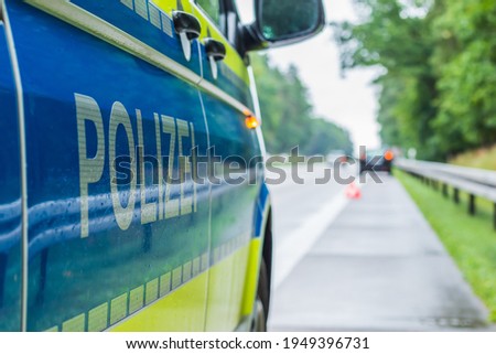 Police car on the highway in a side perspective during an accident. Lettering police on the body with boom and yellow background. Hard shoulder, lane and crash barriers with trees 