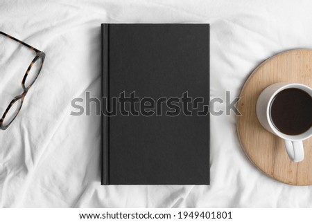 Black book mockup with a cup of coffee and a glasses on the bed. Royalty-Free Stock Photo #1949401801