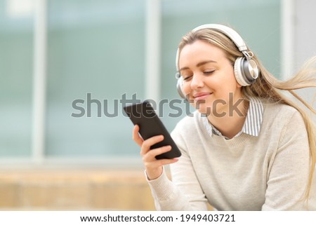 Satisfied teen listening to music on smart phone sitting in the street