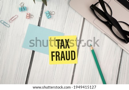 Tax Fraud text on notepad on wooden office desk.