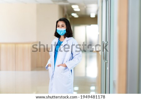 Portrait young and confident Asian female doctor wearing white gown and surgical face mask in hospital. Successful doctor career concept