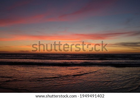 Sunset Sunrise over the ocean with a cloudy sky with soft water long exposure very vibrant sky with pretty colors of purple orange yellow and pink people long walk on beach vacation luxury Monterey CA