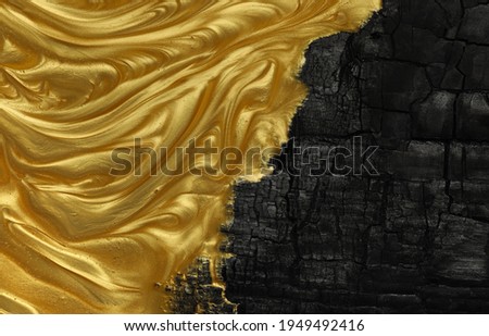 Vivid contrast of black and gold in abstract background of metallic gold paint swirling over charred black ashes.