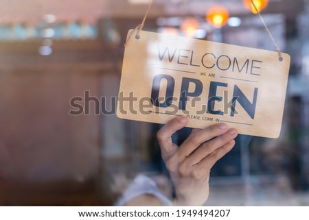 Hand of asian owner retail ,coffee shop woman turning sign board to open. Protection to pandemic of coronavirus. Open store,restaurant or pub due to lockdown quarantine of covid-19.