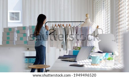 Young attractive beautiful hipster asia female fashion store owner use digital tablet check stock clothes or package box on rail rack at home office small SME business entrepreneur e-commerce concept. Royalty-Free Stock Photo #1949496520