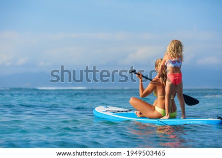 Active paddle boarder at sunset sea. Young mother with little clild paddling on stand up paddleboard. Healthy lifestyle. Water sport, SUP surfing tour in adventure camp on family summer beach vacation Royalty-Free Stock Photo #1949503465