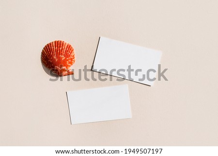 Still life scene with red shell on beige background in sunlight and blank business, greeting card, invitation mockup. Long harsh shadows. Flat lay, top view.