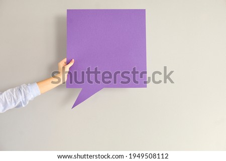 Young anonymous woman or teen girl holding one clean violet square shaped free mockup copyspace speech bubble in hand on gray background. Blank card for message, quote, inspiration, expressing opinion