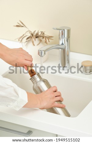 Woman washes a metal reusable bottle with a coconut brush. Washing dishes without chemicals. Reusable eco-friendly kitchen products. Zero waste and sustainable plastic free lifestyle.  Royalty-Free Stock Photo #1949515102